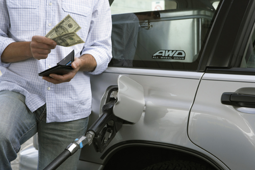Man pumping gas into his car with cash in his hand.